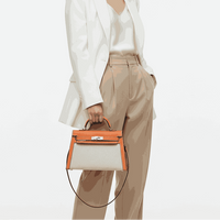 Woman in a white blazer and beige pants holding a Hermès bag on a white background